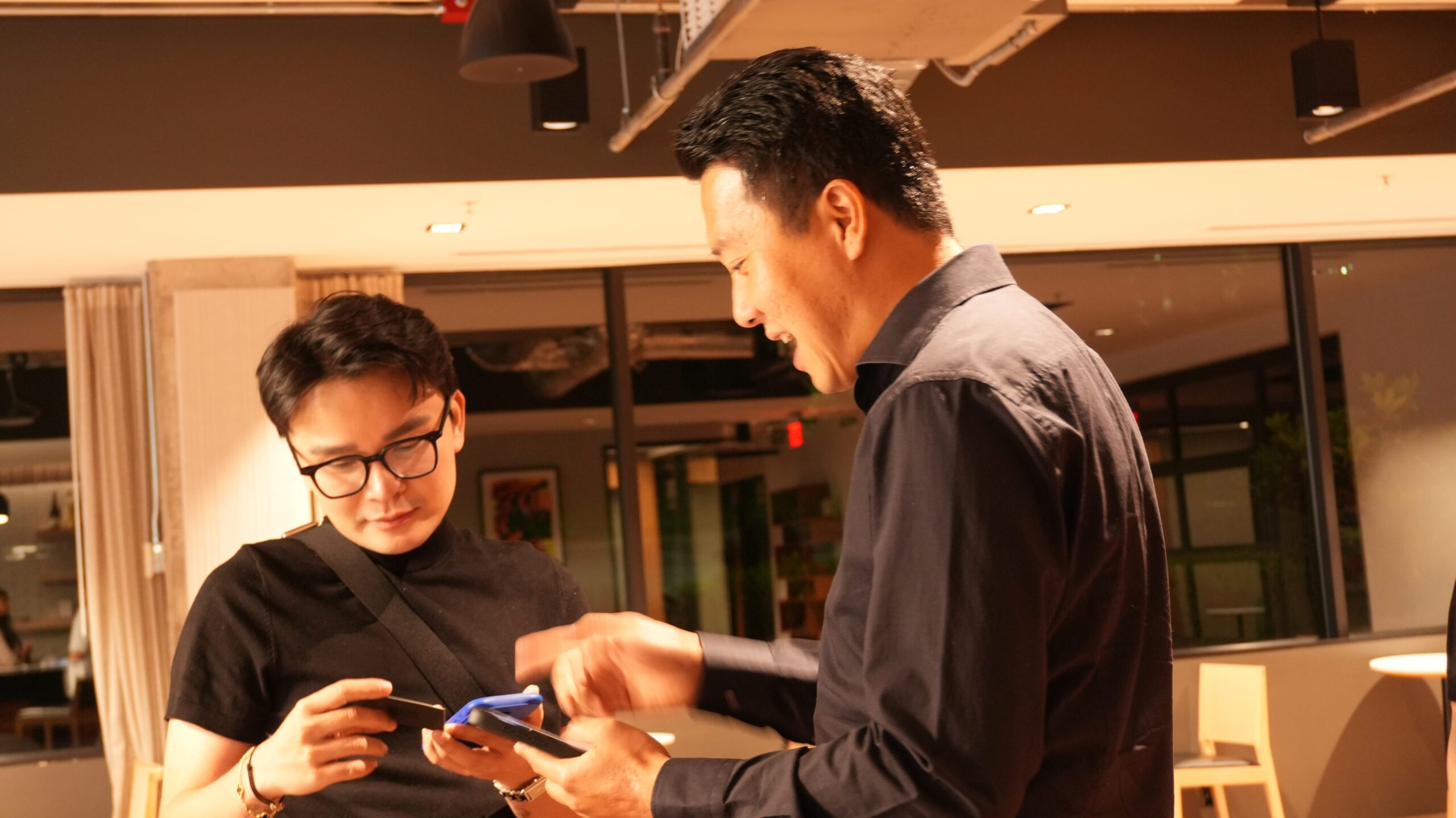 Two businessmen engage in conversation while looking at a device, representing a business meeting or agreement related to the **THM Offices** partnership.