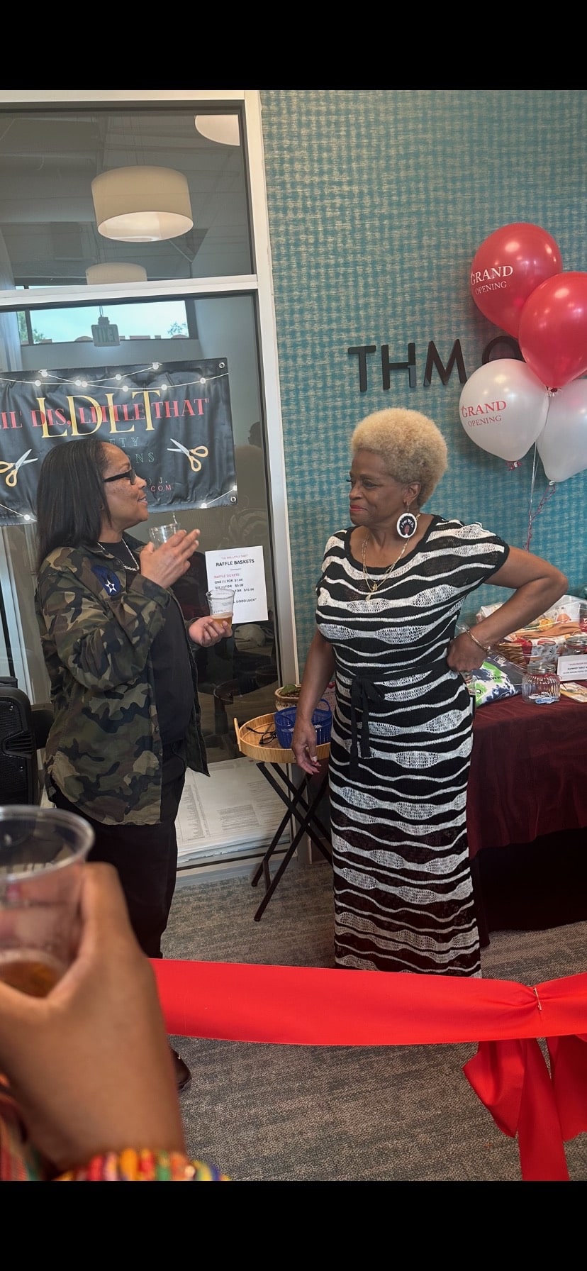 Two women talk near a table with balloons at a grand opening event for **THM Offices**, showcasing the community aspect of the managed property.