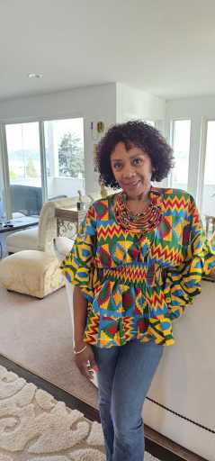 A woman in traditional African print stands in a modern, bright apartment with large windows, representing a successful tenant or partner. 